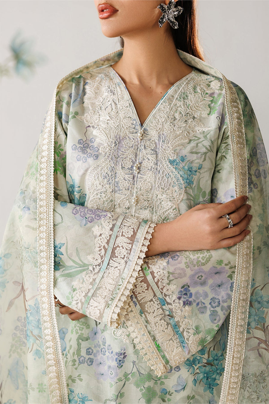 Close-up of embroidered neckline featuring delicate floral lace pattern and pearl embellishments on pastel lawn fabric