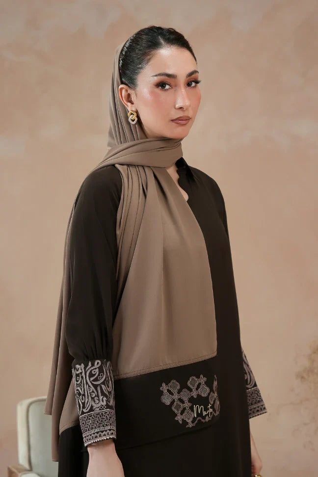 Woman wearing a modest taupe scarf draped elegantly over her head and shoulders, paired with a black outfit featuring embroidered cuffs and hem.