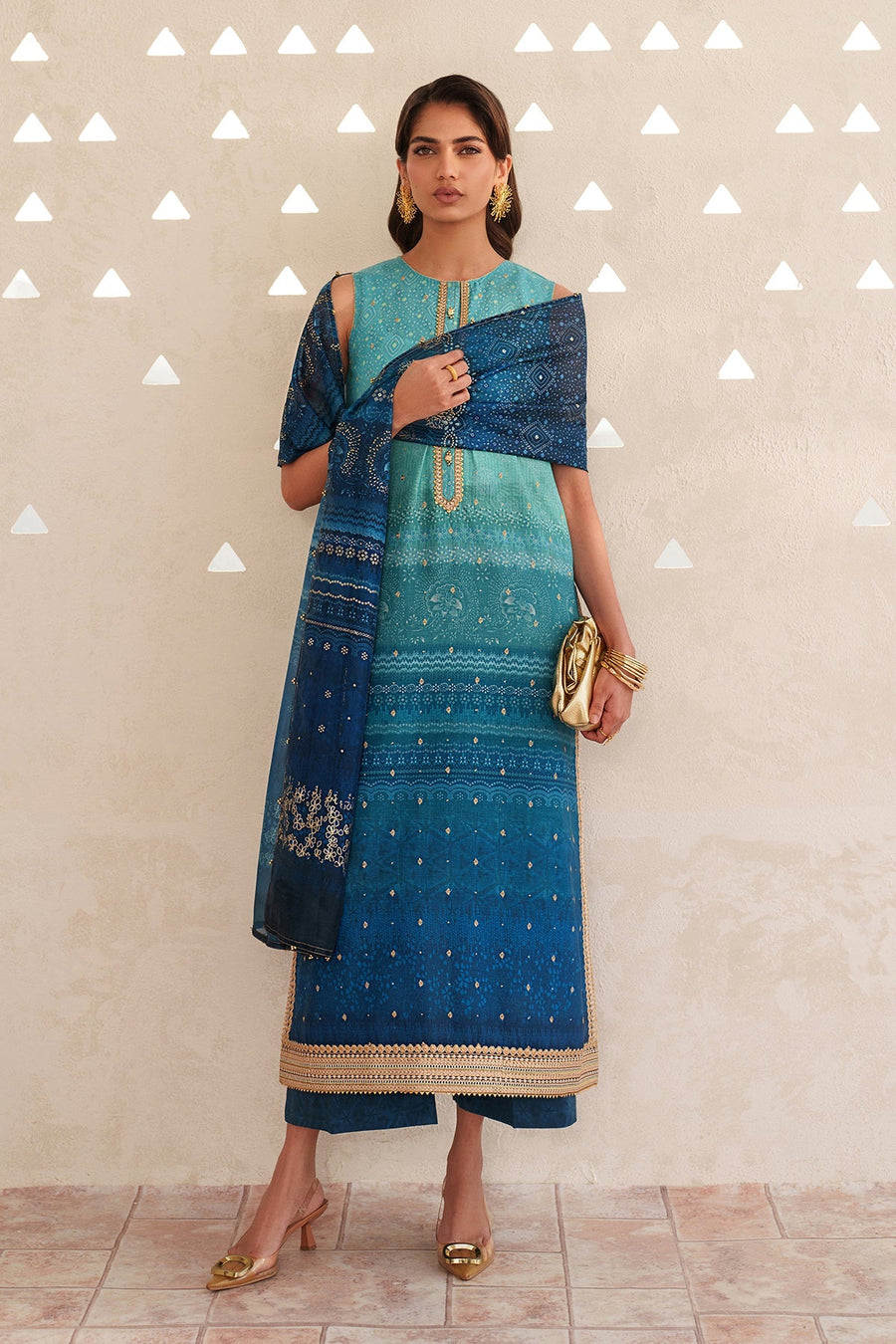 Full frontal view of the sleeveless ombre lawn suit combined with the printed dupatta and golden accessories standing on tiled floor