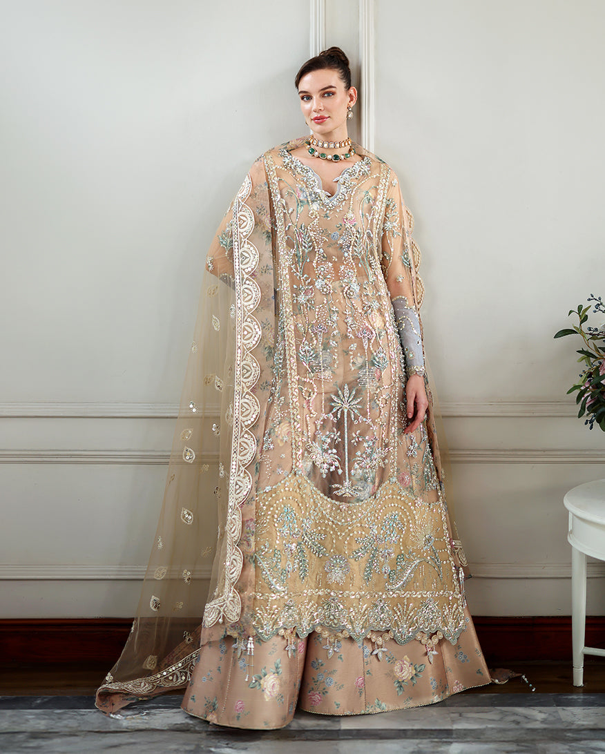 Model wearing elegant beige net formal dress with heavy floral embroidery, sequins, and detailed scalloped hem matching wide-legged pants and sheer dupatta