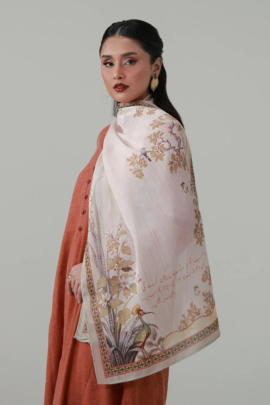 Woman wearing a Titli silk scarf draped elegantly over her shoulder, featuring floral and bird motifs with calligraphy on a light background.