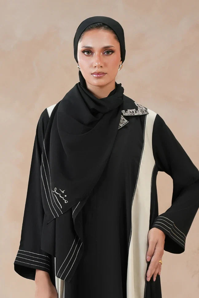 Woman wearing a sleek black scarf with delicate ivory embroidery in Urdu calligraphy, paired with a stylish black and white embroidered outfit.