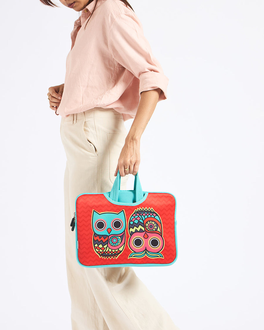 Woman holding a colorful laptop sleeve with a turquoise and red owl print and turquoise handles against a white background.