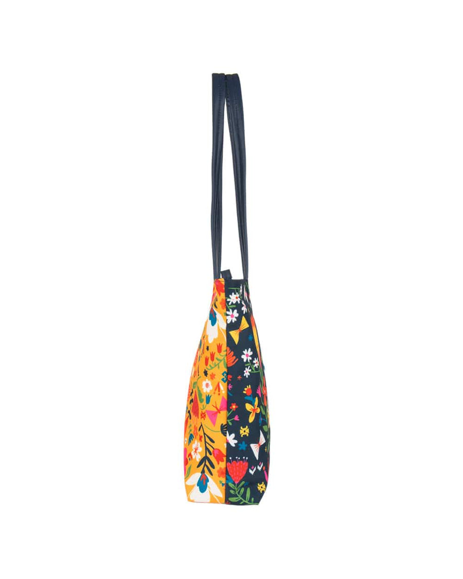 Side profile of tote bag with navy blue handles and colorful floral patterns