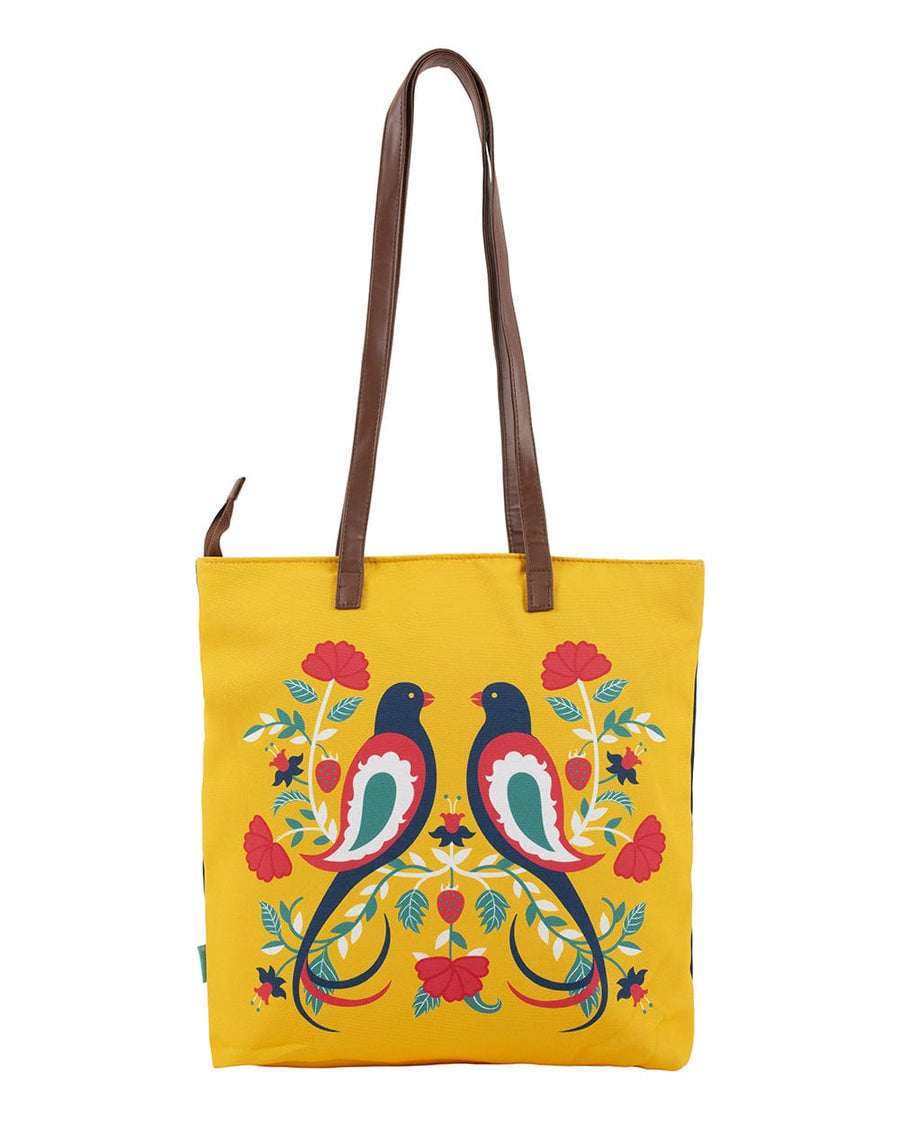 Reversible tote bag shown in bright yellow side with matching colorful bird and floral design and brown leather-like shoulder straps