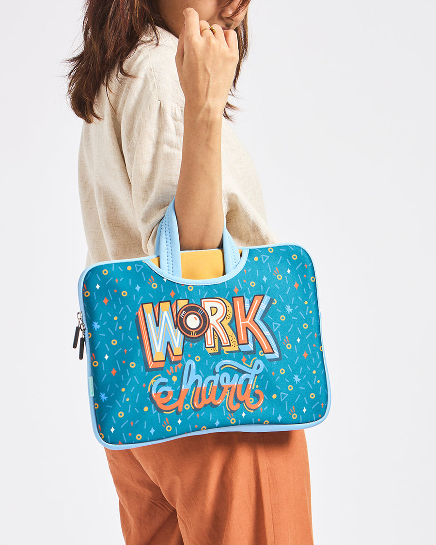 Woman holding blue neoprene laptop sleeve with colorful Work Hard lettering and geometric patterns