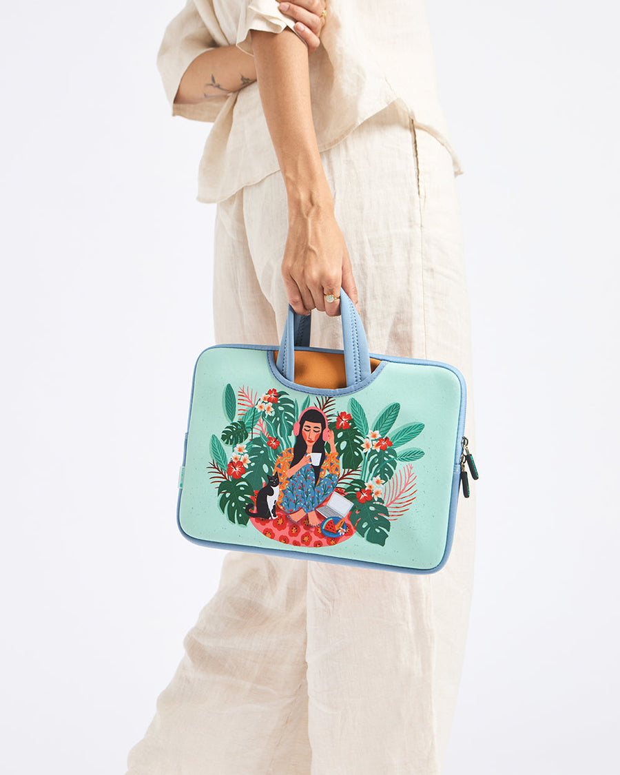 Woman holding pastel blue laptop sleeve bag with colorful artwork of a woman surrounded by tropical leaves and flowers