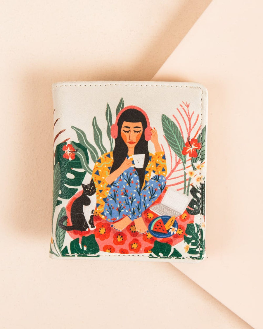 Mini wallet with colorful hand-painted design showing a woman with headphones drinking tea, a black cat, a laptop, and tropical plants on a cream background