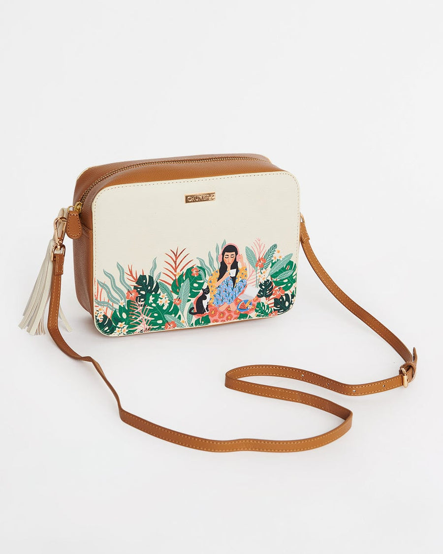 Elegant ivory sling bag with brown adjustable strap and artistic floral print featuring a woman surrounded by greenery