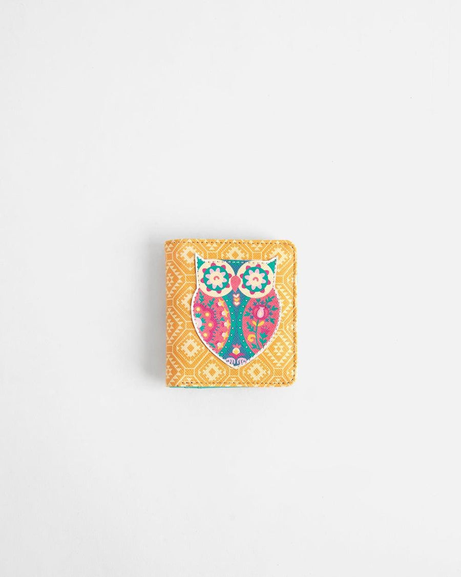 Compact mustard-yellow wallet featuring colorful embroidered owl applique on front with geometric pattern background