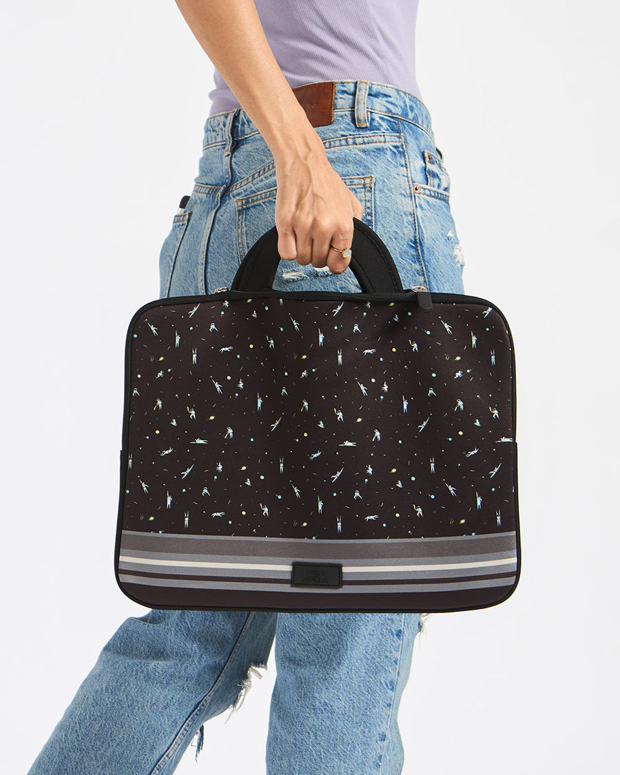 Hand holding a black Milky Way Laptop Sleeve with cosmic pattern and gray stripes, paired with casual denim jeans.