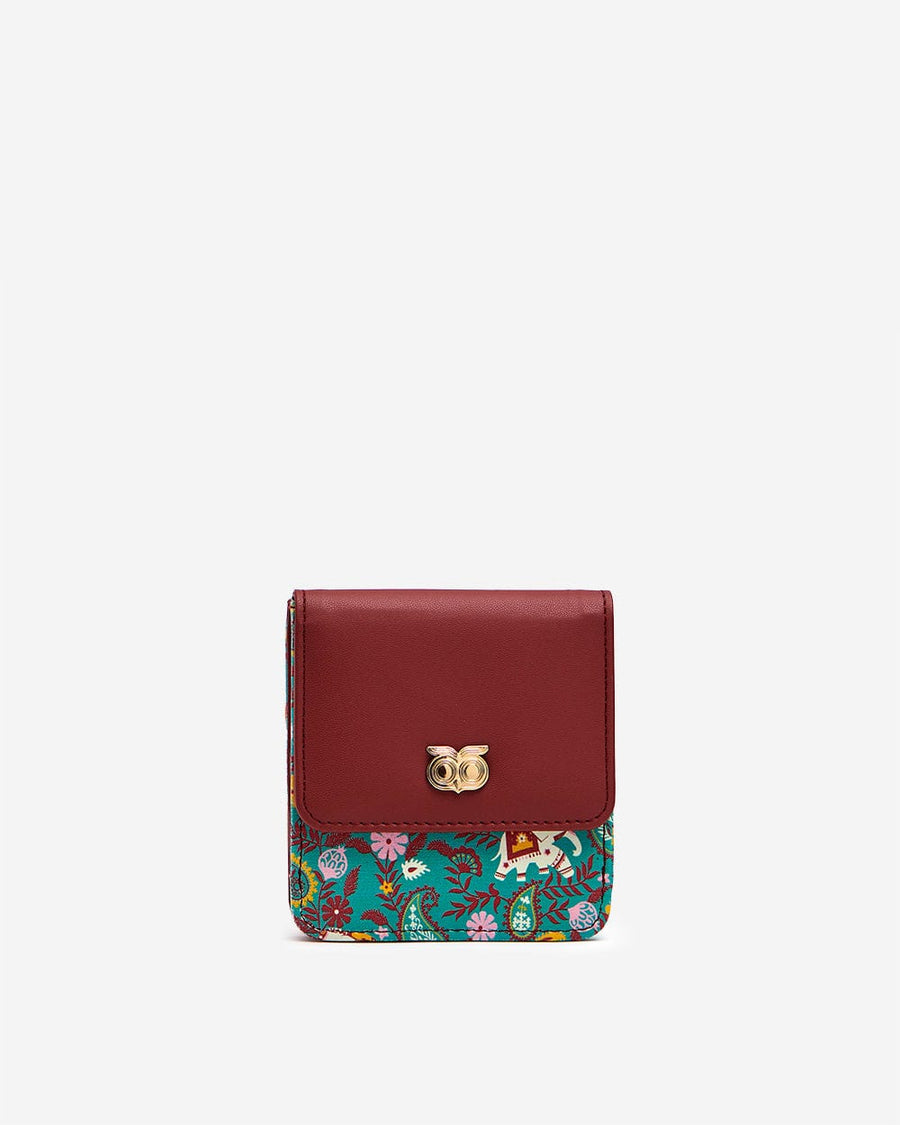 Front view of a compact women's wallet with maroon faux leather flap and multicolor paisley fabric featuring floral and elephant prints, accented by a gold-tone owl emblem.