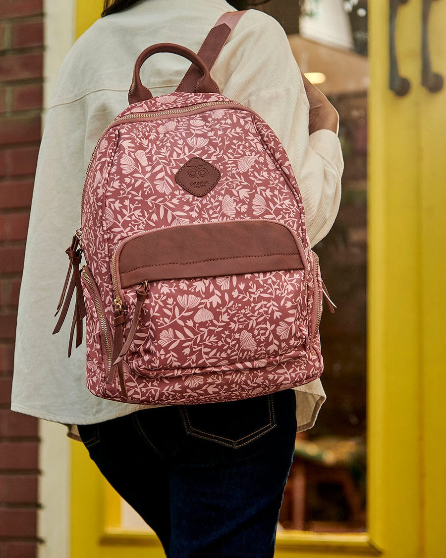 Woman carrying dusty rose pink floral patterned backpack with faux leather front pocket and adjustable straps outdoors