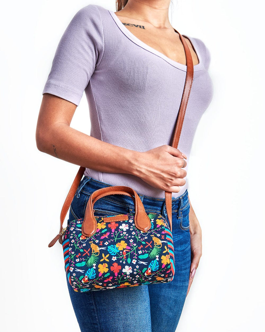 Woman wearing a colorful floral sling bag with brown leather strap and handles paired with casual jeans and lavender top