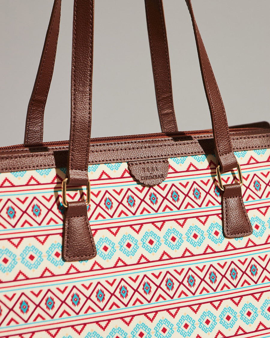 Close-up of the tote’s brown vegan leather handles attached with gold-toned metal rings to the Aztec print body