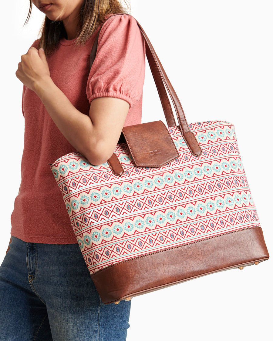 Woman wearing pink shirt carrying an Aztec patterned tote bag with brown faux leather handles and trim