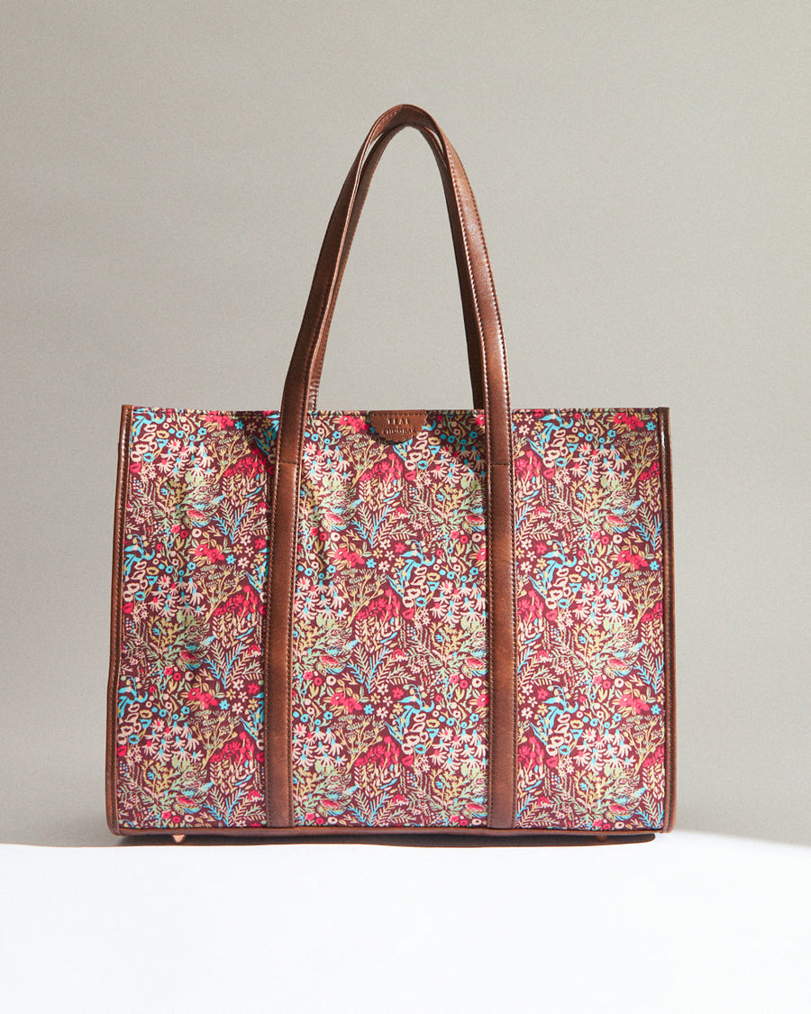 Front view of colorful floral canvas tote bag with brown vegan leather handles and trims against neutral background