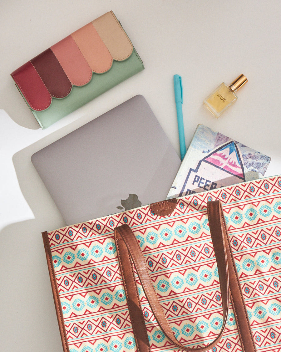 Top-down view of the tote bag partially filled with a laptop, colorful wallet, notebook, pen, and perfume bottle