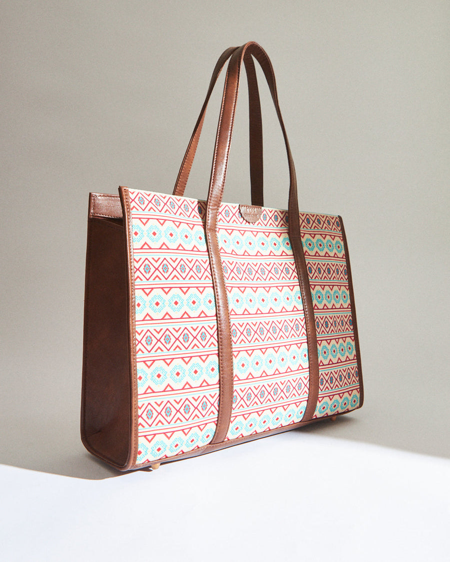 Diagonal side view highlighting the bag's structure, patterned canvas front, and brown vegan leather sides and handles