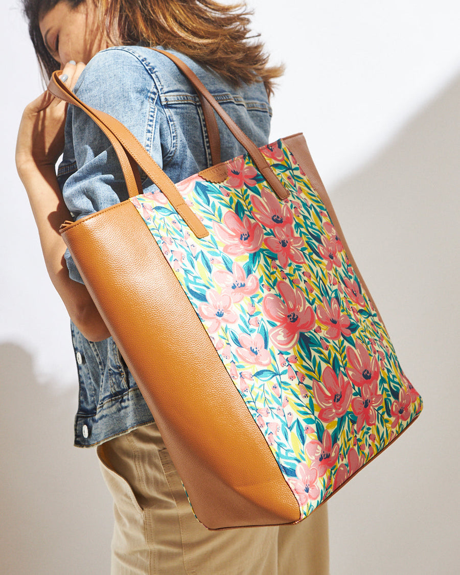 Woman wearing a floral pattern tote bag with tan faux leather sides and straps over a denim jacket