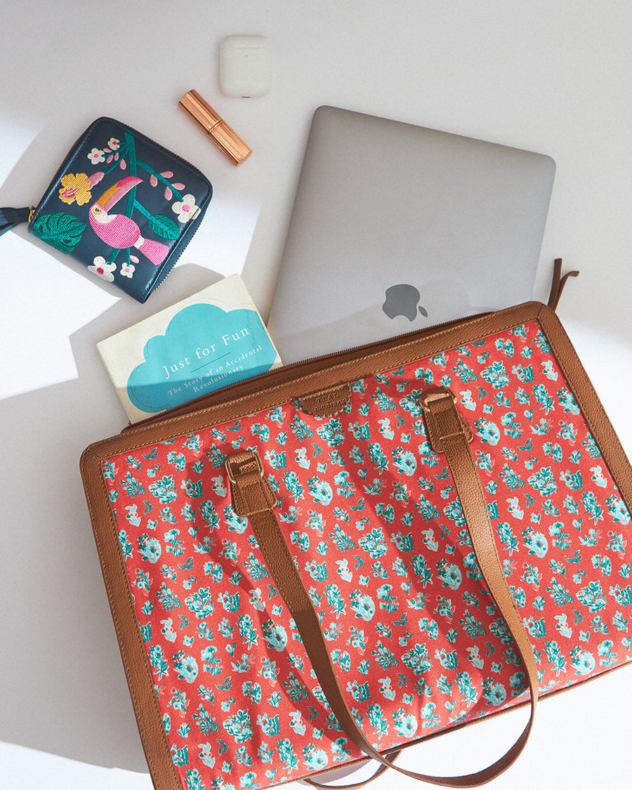 Overhead flat lay of red floral tote bag partially open revealing laptop, book, AirPods case, and embroidered pouch
