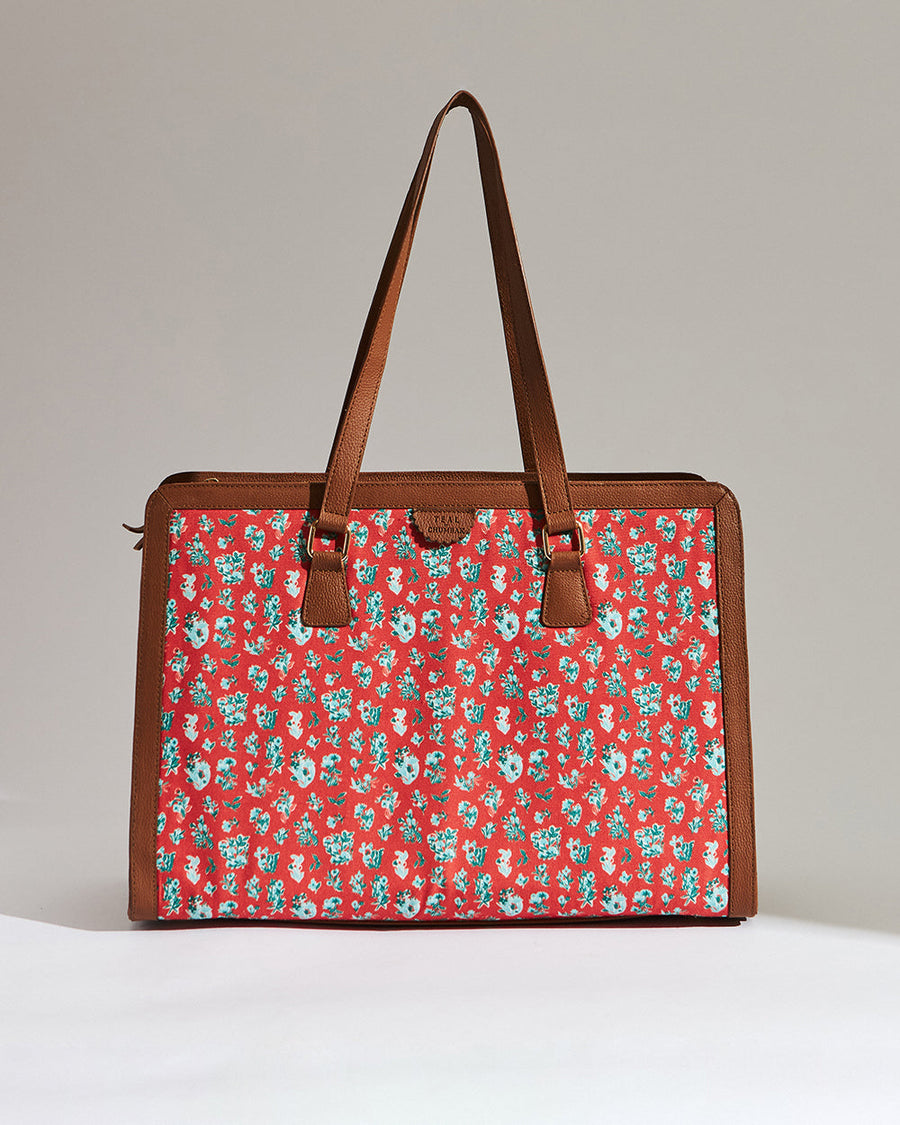 Straight-on view of red floral canvas tote bag bordered with brown vegan leather handles on a light background