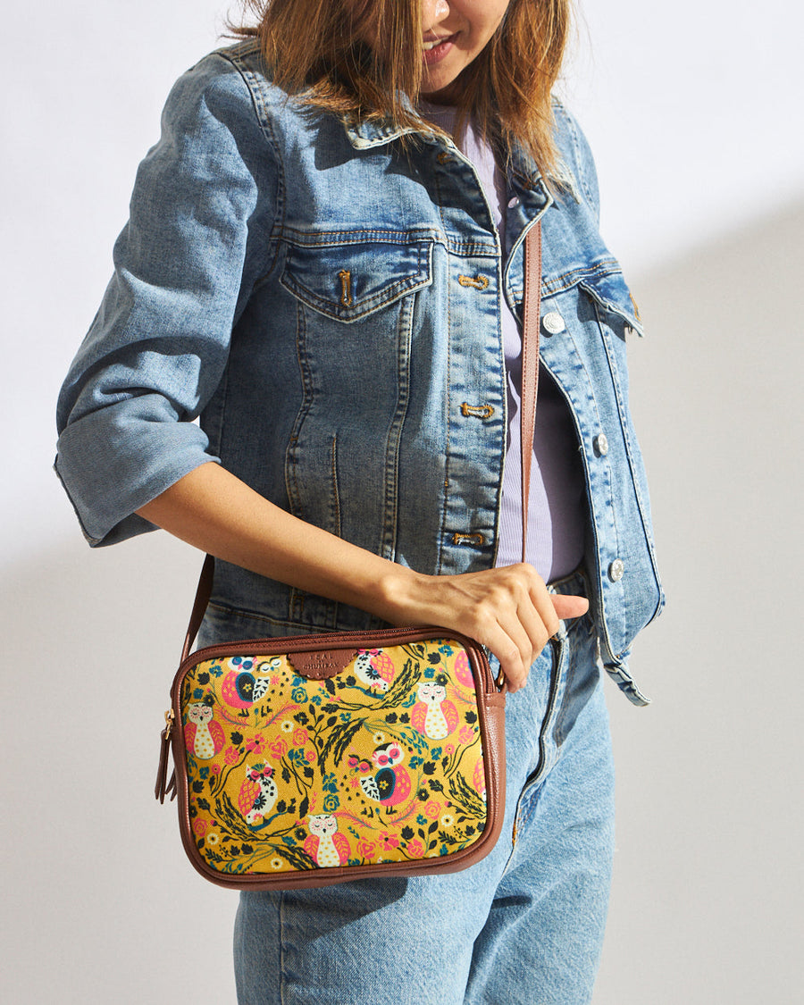 Woman wearing denim jacket and jeans with Teal Jungle Stories yellow crossbody bag featuring colorful owl and floral print