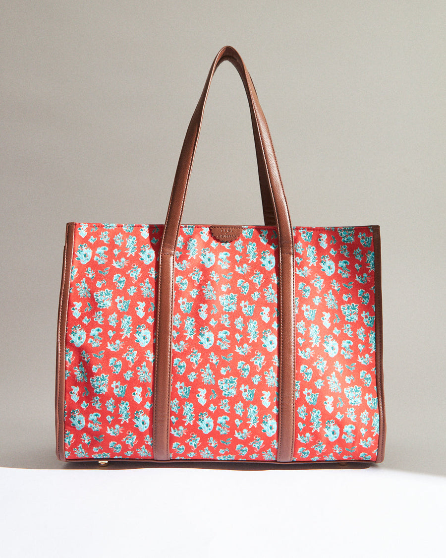 Red canvas tote bag with light blue and white floral pattern and brown leather handles and trim