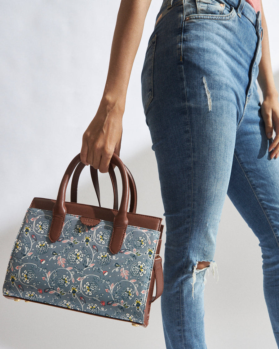 Woman holding a teal floral canvas handbag with brown vegan leather handles and accents, paired with blue jeans