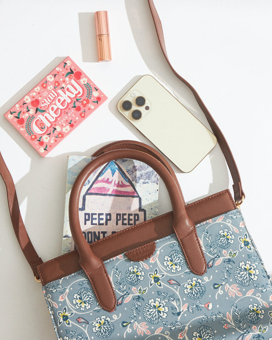 Top view of teal floral canvas handbag showing contents including smartphone, makeup, face kit, and book