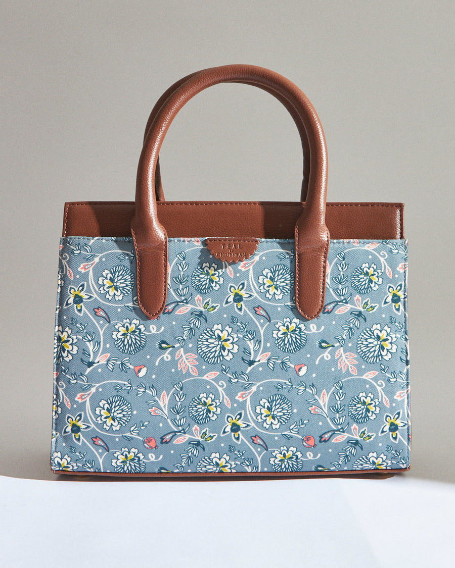 Front view of teal floral canvas handbag with brown vegan leather handles and floral pattern
