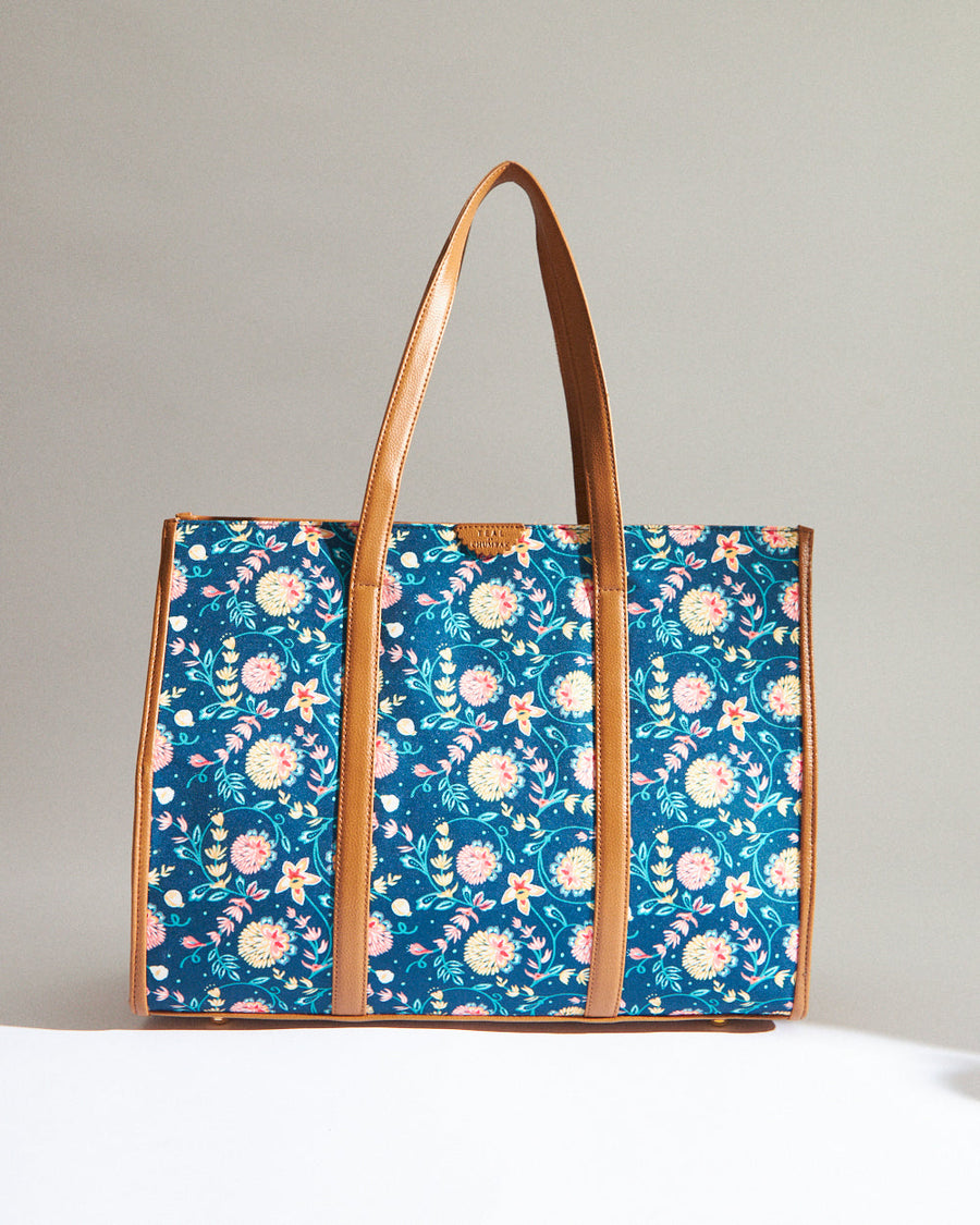 Dark blue canvas tote bag with pink and yellow floral pattern and brown leather handles and trim