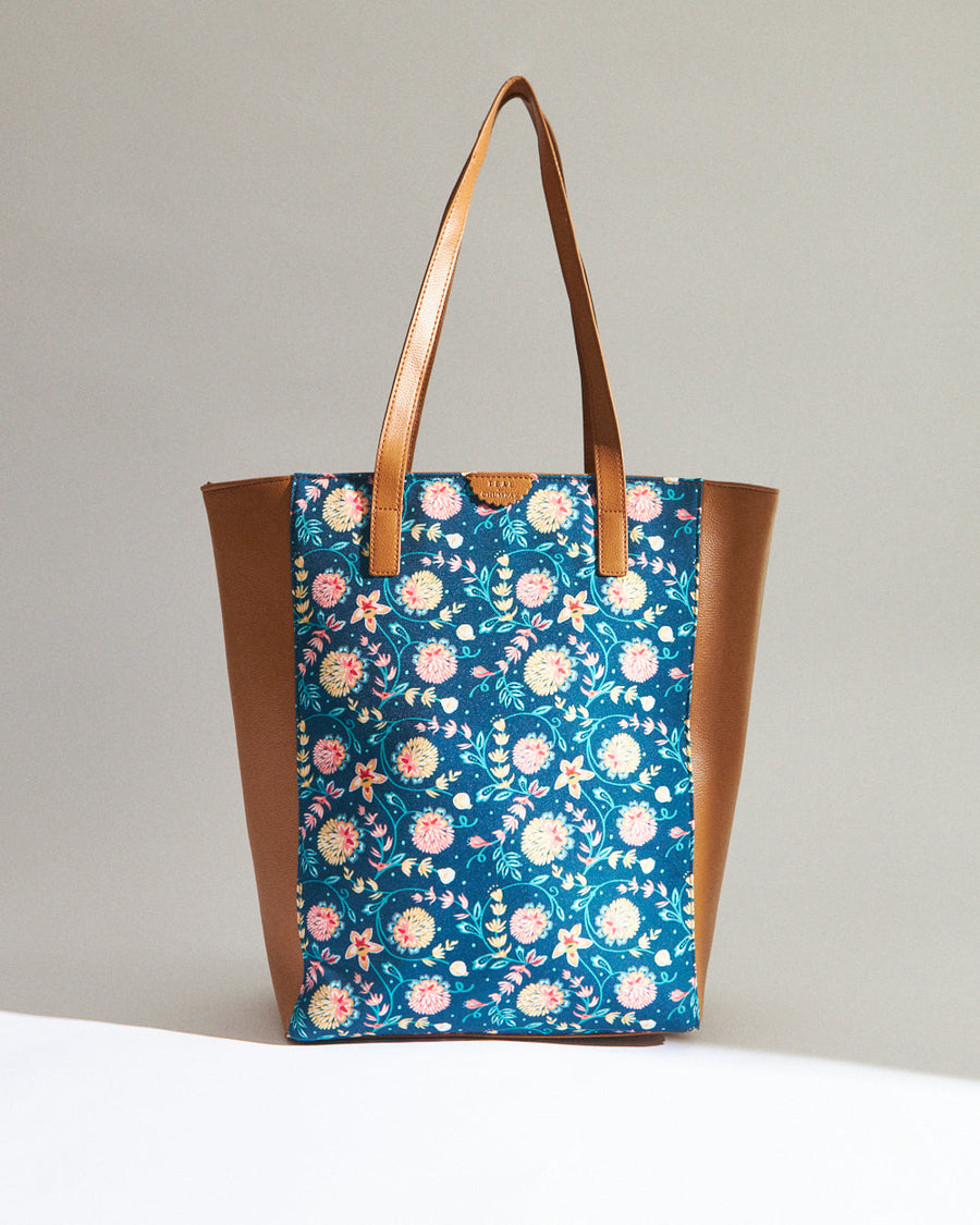 Front view of blue floral canvas tote bag with tan vegan leather sides and straps