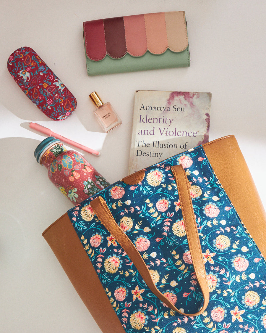 Tote bag laid flat surrounded by women's accessories including wallet, perfume, and water bottle