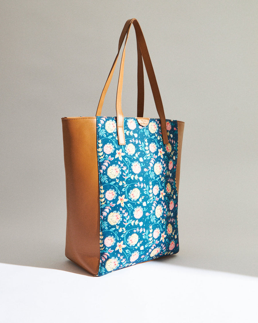 Side profile of blue floral print vegan leather tote bag with camel sides resting upright