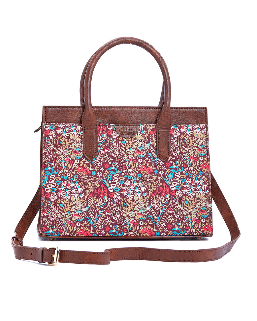 Dark brown leather handbag adorned with maroon fabric covered in a botanical multi-color spread with strap