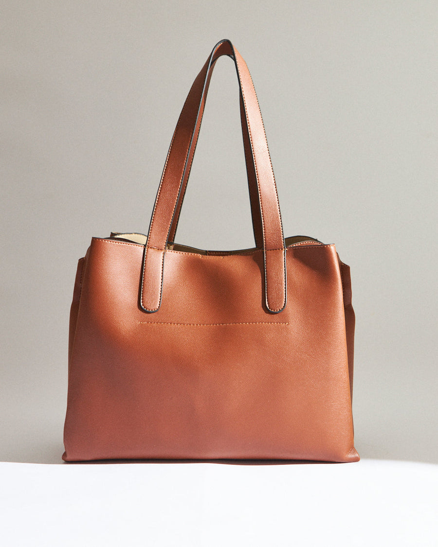 Back view of a plain tan tote bag showing smooth faux leather surface and attached shoulder straps