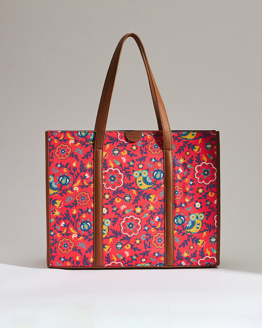 Red floral print canvas tote bag with green leaves, accented with brown leather handles and trim