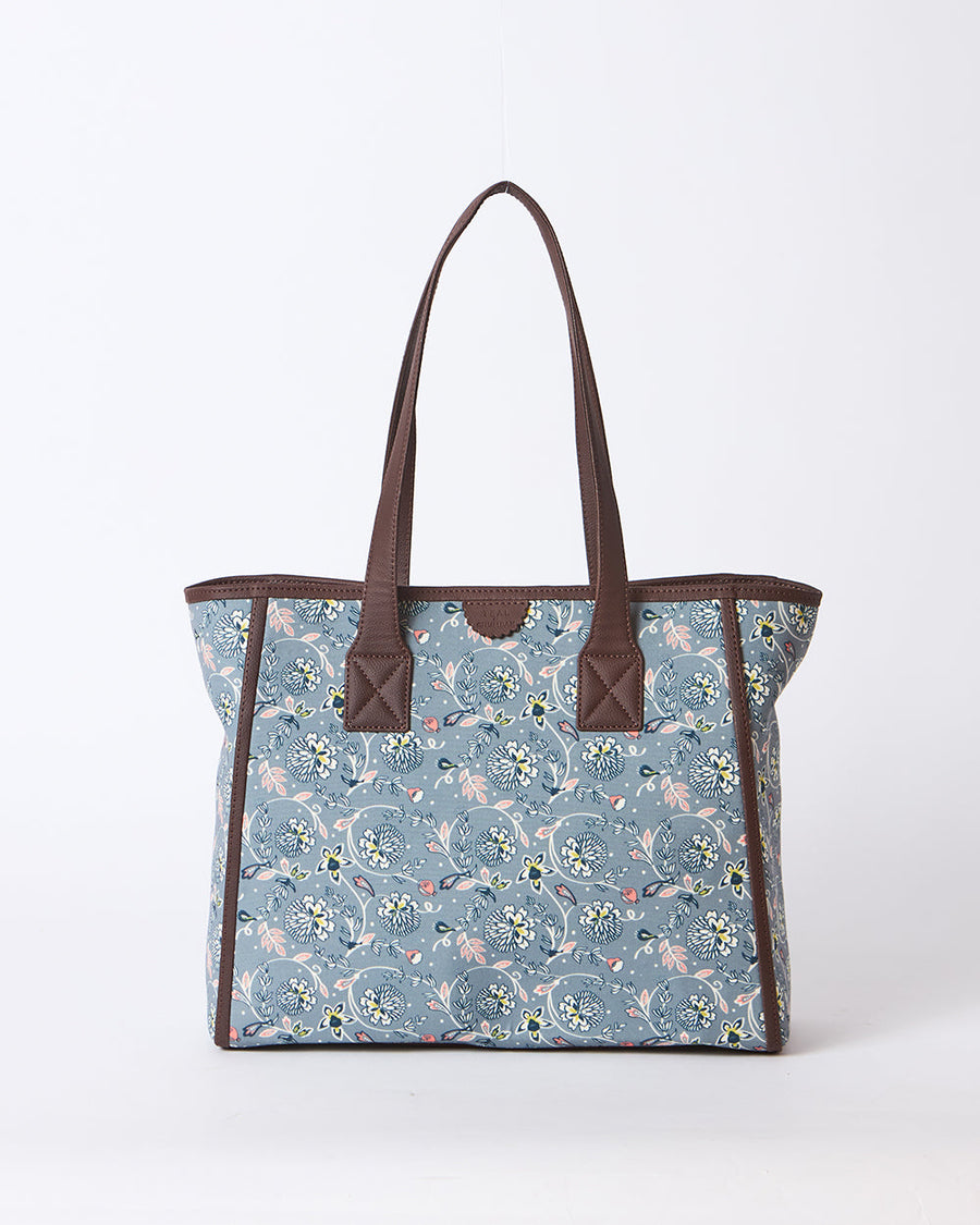 Front view of floral canvas tote bag with brown faux leather handles and trim against white background