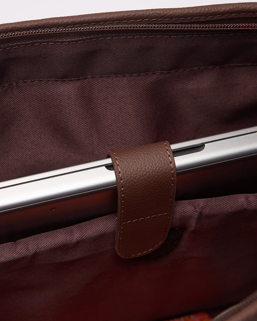 Interior close-up of padded laptop slot holding a laptop, secured with brown faux leather strap