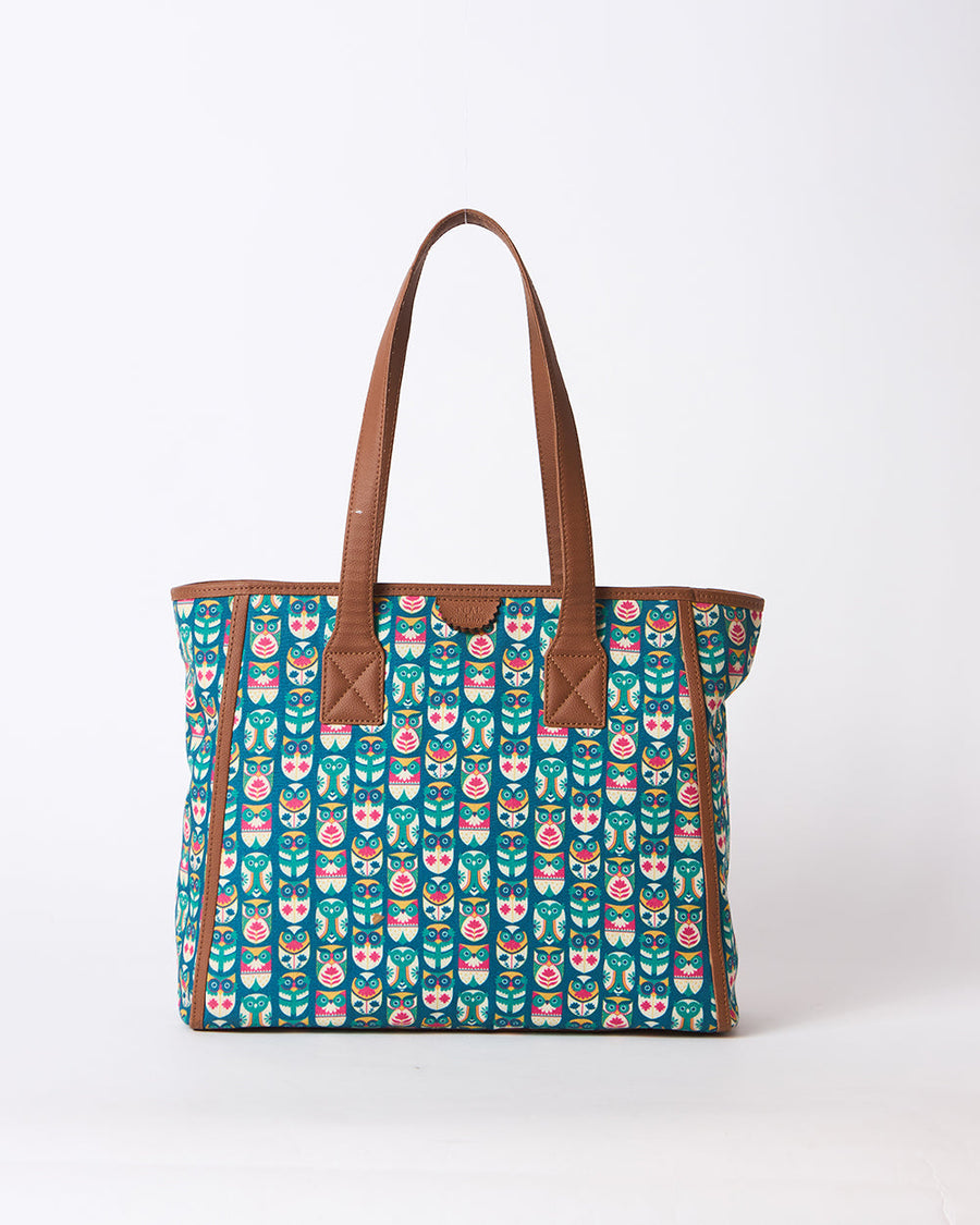 Teal canvas tote bag featuring colorful owl prints with brown faux leather handles and trim, photographed on white background.