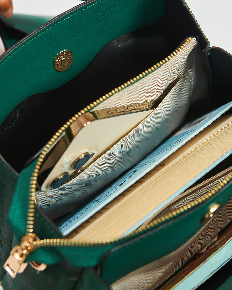 Interior close-up of emerald handbag displaying zipper pocket with items inside, detailed lining and snap button closure