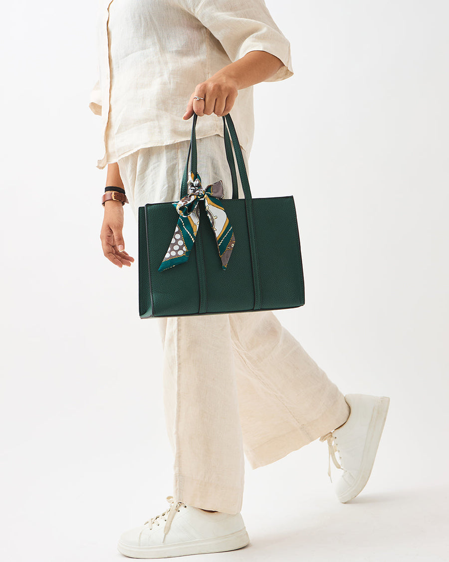 Woman wearing cream outfit holding green mini tote bag with printed scarf tied to handle