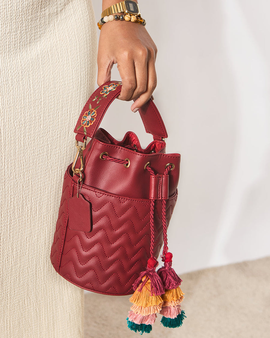 Woman holding embroidered bucket bag by padded floral embroidered handle against beige dress