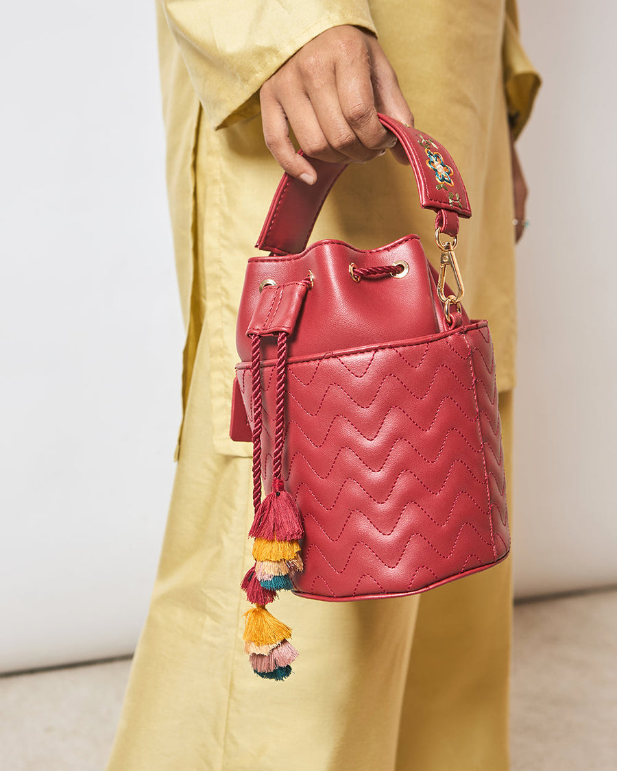 Close-up showing embroidered red bucket bag held by hand, highlighting tassels and quilting