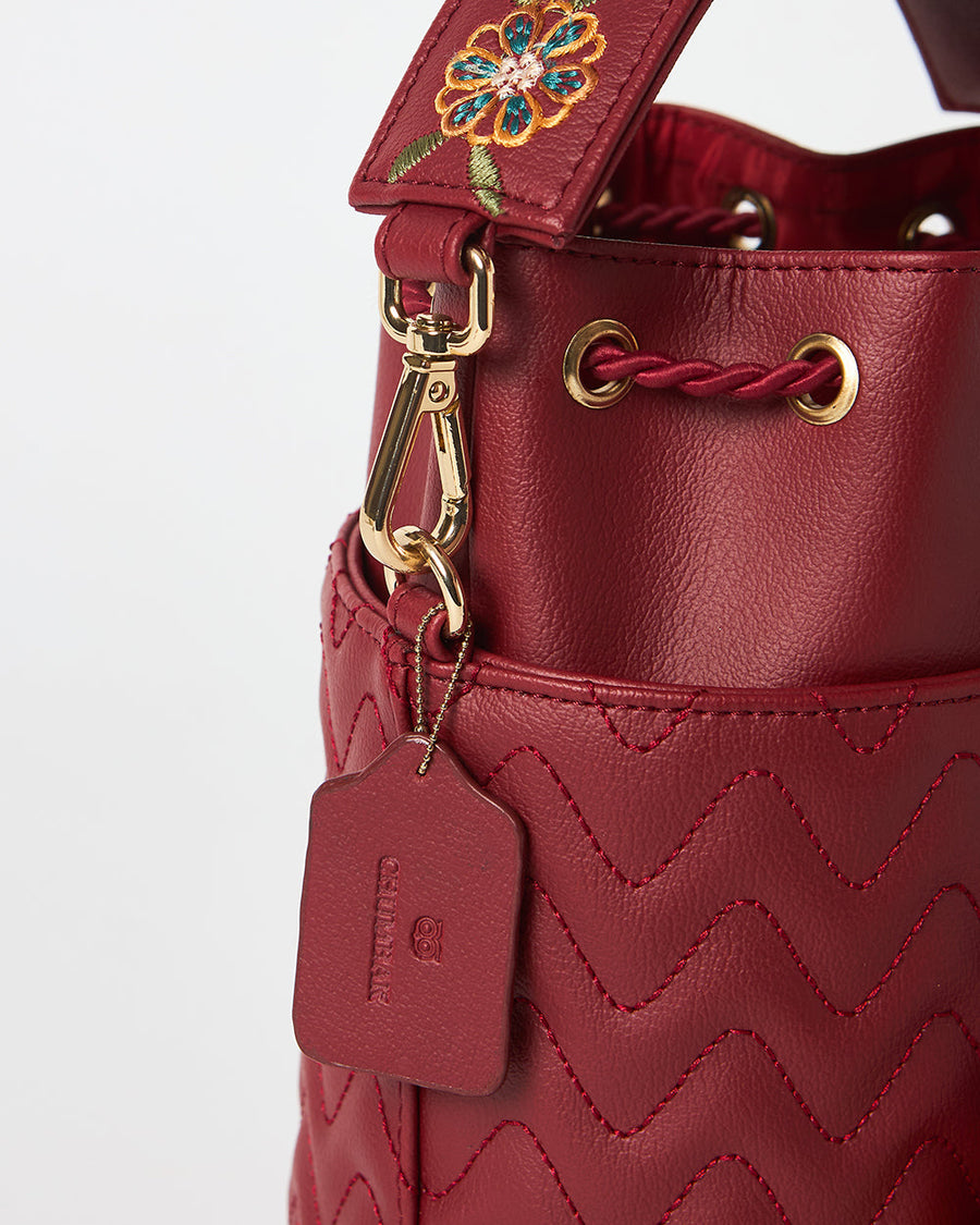 Detail image showing gold clip and branded leather tag attached to red bucket bag