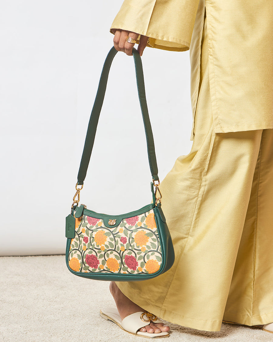 Woman holding an elegant shoulder bag with floral embroidery in orange and rose pink tones, featuring green leather accents and gold hardware