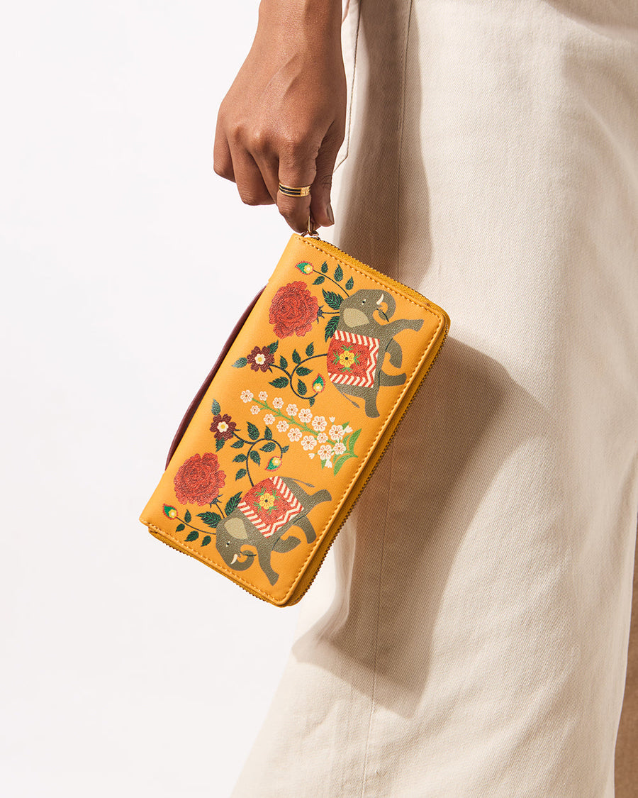 Close-up of woman holding mustard yellow wallet with elephant and floral motif against white pants