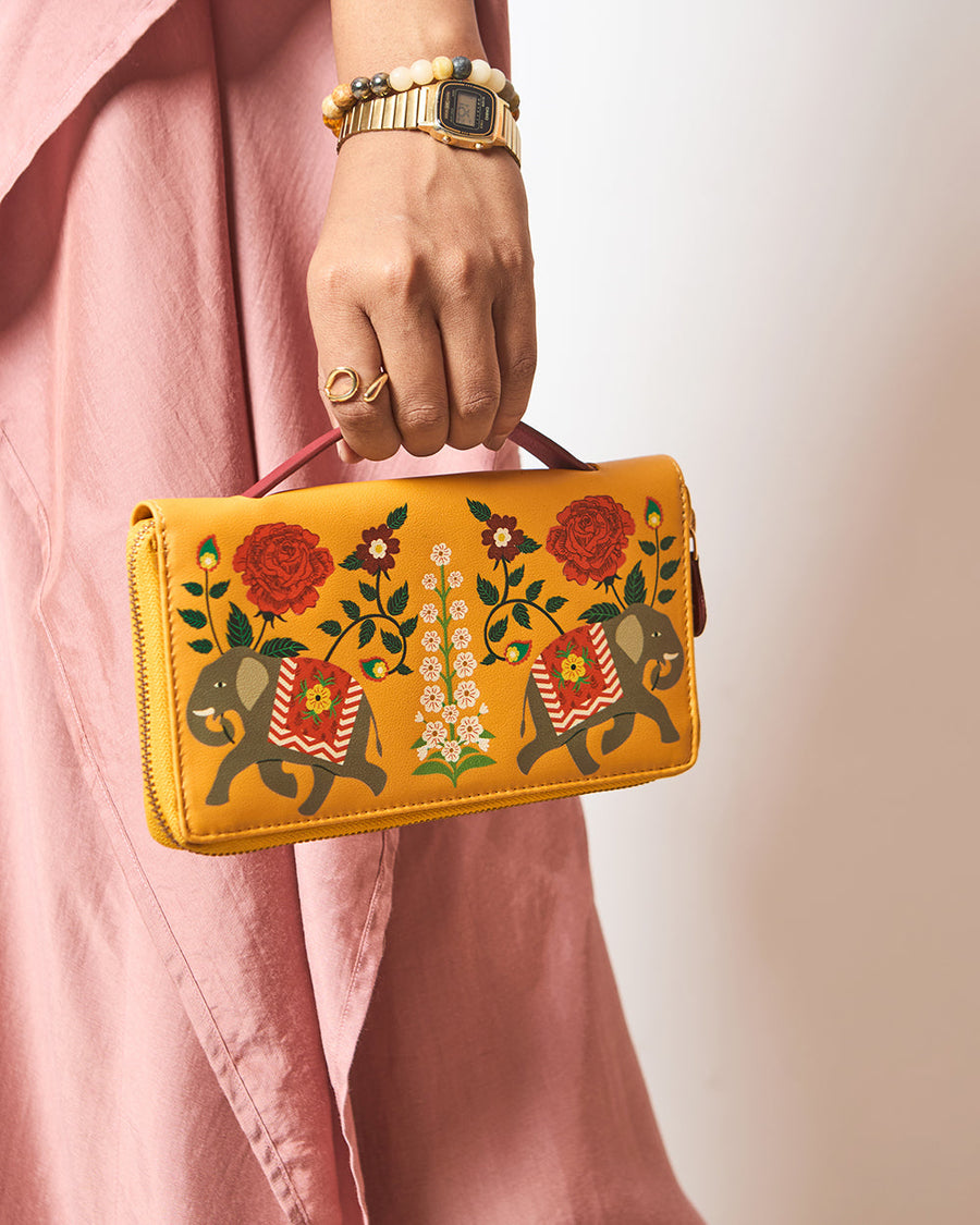 Woman holding mustard yellow wallet with elephant and floral print in front of pink linen outfit