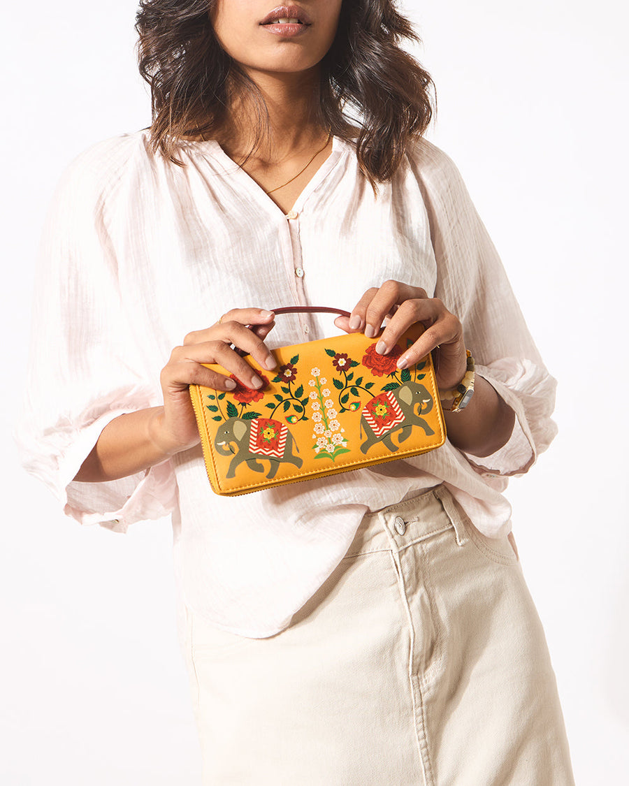 Front view of woman holding royal elephant motif wallet in white top and beige pants